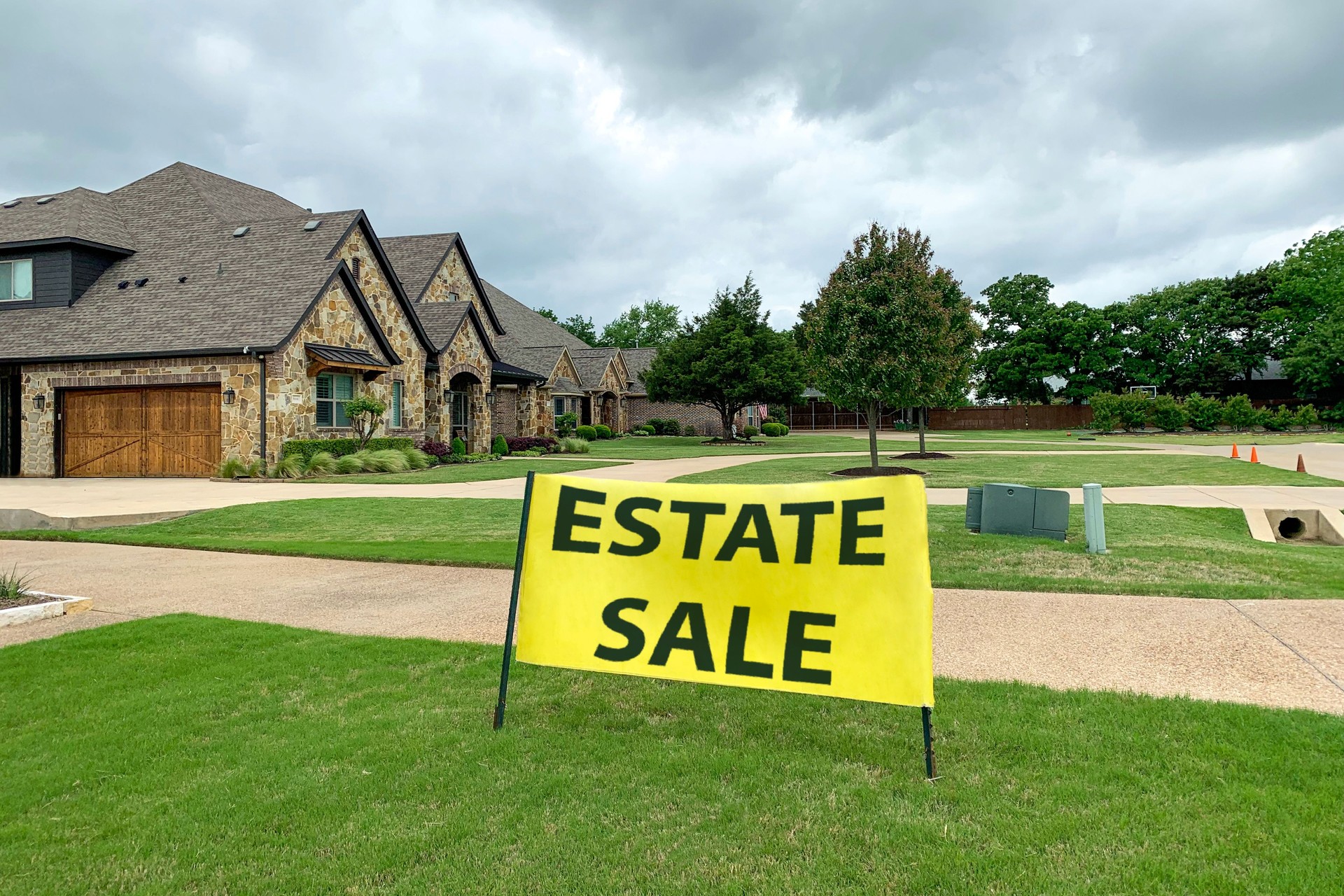 Residential house with road and neat lawn in front, big yellow sign with estate sale inscription.